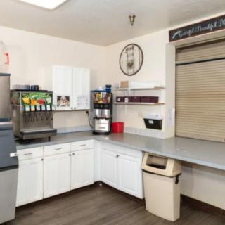 A clean cafeteria kitchen area with a soda dispenser, coffee machine, and storage cabinets.