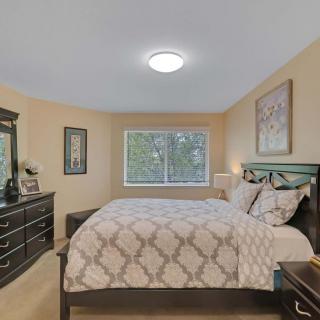 A cozy bedroom with a large bed, dresser, and window adorned with wall art.