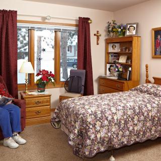 A cozy bedroom featuring a single bed, wooden furniture, and a window with curtains.