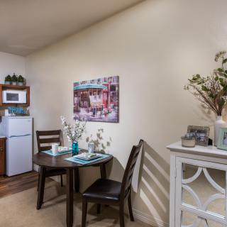 A cozy kitchen and dining area featuring a small table with chairs, a refrigerator, microwave, and decorative elements.
