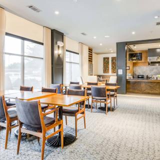 A modern dining area with wooden tables and chairs, featuring large windows and comfortable seating.
