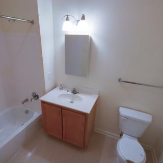 A clean and simple bathroom with a bathtub, sink, cabinet, toilet, and mirror.