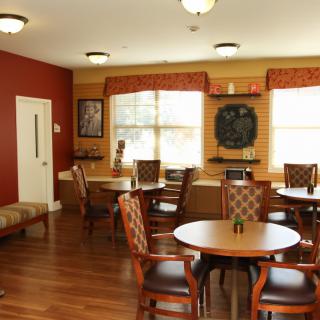 A cozy dining area with round tables and chairs, featuring warm decor and large windows.