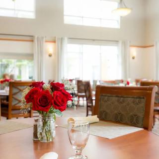 A bright and inviting dining room with elegantly set tables, featuring vases of red roses as centerpieces.