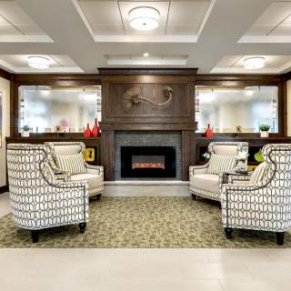 A cozy and elegant living room with patterned chairs arranged around a fireplace, complemented by wood paneling and elegant lighting.