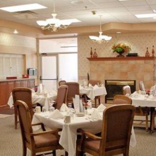 A cozy dining room setup with elegantly arranged tables and chairs, featuring a welcoming fireplace and warm lighting.