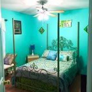A cozy bedroom with turquoise walls, featuring a four-poster bed and ceiling fan.