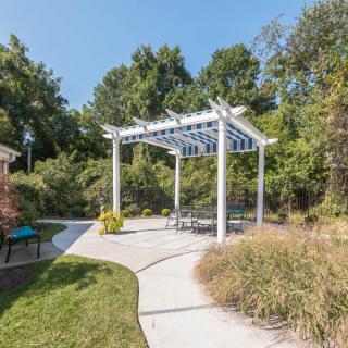 A peaceful garden setting featuring a white pergola with seating, surrounded by lush greenery and a winding pathway.