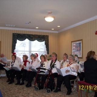A group of people in holiday attire singing indoors, likely a choir performing during the Christmas season.