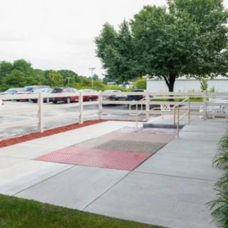 A fenced area by the sidewalk next to a parking lot with trees in the background.