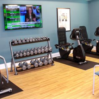 A modern gym setup with dumbbells, exercise bikes, and a television on the wall.