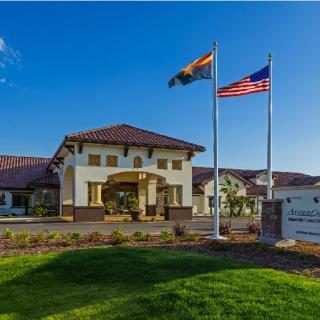 A building with a prominent entrance, surrounded by a well-kept lawn, with two flags flying under clear blue skies.