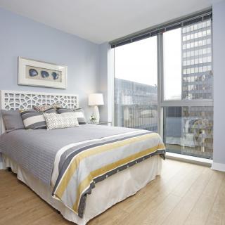 A modern bedroom with large windows offering a city view and ample natural light.