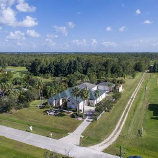 Aerial view of a large house in a rural setting surrounded by open fields and trees.