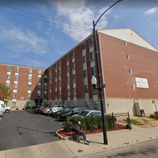 A multi-story brick building with a parking lot and cars in an urban area during the daytime.
