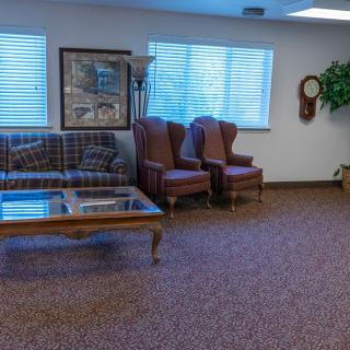 A waiting room with a sofa, chairs, and coffee table arranged on a carpeted floor.