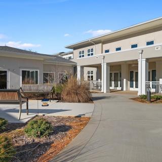 A modern building with a wide pathway and landscaped surroundings under a clear blue sky.