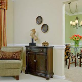 A cozy living room corner featuring a wooden cabinet with decorative items, adjacent to a dining area with a chandelier and floral centerpiece.
