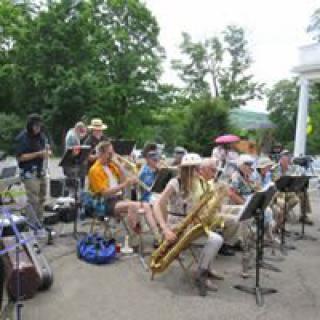 A band performs outdoors with various musicians playing instruments like saxophones in a wooded area.