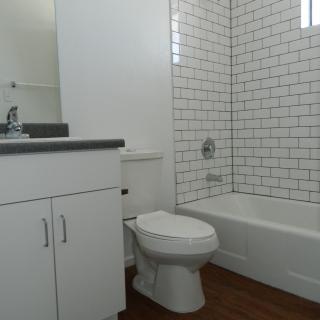A modern bathroom with white subway tiles, featuring a bathtub, toilet, and sink.