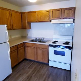 A small apartment kitchen with wooden cabinets, a white refrigerator, oven, and stove.