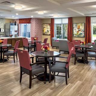 A cozy dining area with neatly arranged tables and chairs, featuring large windows and warm decor.