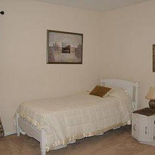 A cozy bedroom featuring a single bed with a cream-colored duvet, complemented by a nightstand and lamp. A framed picture decorates the wall.