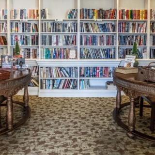 A cozy library with bookshelves filled with a variety of books and comfortable wooden desks for reading.