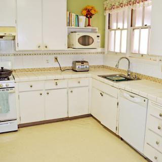 A retro-style kitchen with white cabinets, a microwave, a toaster, and a stove.