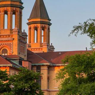 A beautiful church with twin towers bathed in the warm light of sunset, surrounded by lush trees.