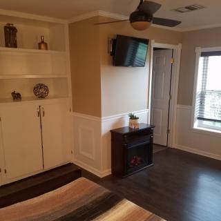 A cozy bedroom with a wall-mounted TV, built-in shelves, and a large window.