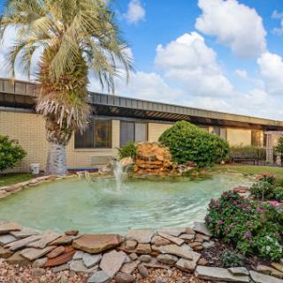 A serene garden with a fountain, surrounded by lush greenery and a beautiful sky.