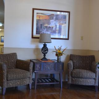 A cozy seating area featuring two patterned chairs, a small table with a lamp, and a decorative piece.