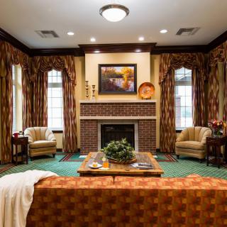 A cozy and traditionally styled living room with a central fireplace, elegant drapes, and comfortable seating.
