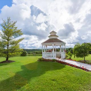 A picturesque gazebo surrounded by lush greenery under a partly cloudy sky.