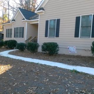 A beige house with a front walkway and neatly trimmed shrubs.