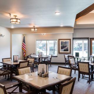 A modern dining room with multiple tables and chairs, featuring large windows and elegant lighting.