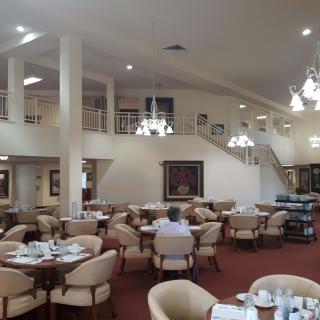 An elegant and spacious restaurant dining area with chandeliers and neatly arranged tables and chairs.