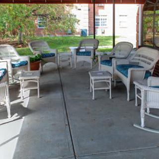 A cozy outdoor seating area with wicker furniture and blue cushions, situated under a covered patio.