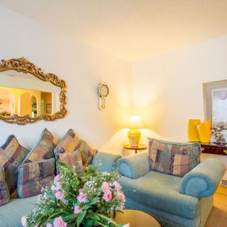 A cozy living room featuring a comfortable sofa adorned with patterned cushions, a decorative mirror, and a soft-lit lamp on the side table.