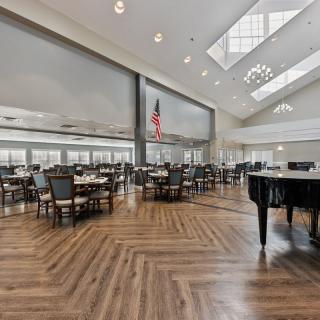 A spacious dining area with elegant furniture and a grand piano, illuminated by natural light from skylights and large windows.