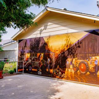 A vibrant mural featuring firetrucks covers the side of a garage next to a driveway, surrounded by trees.