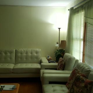 A cozy living room featuring a corner sofa and floor lamp next to a window with curtains.