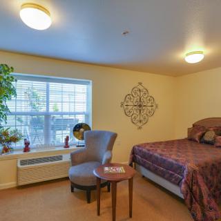 A cozy bedroom featuring a bed, a comfortable chair, and natural light coming through the window.