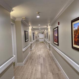 A well-lit hallway with paintings on the walls and wooden flooring.