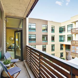 A modern apartment balcony with outdoor seating and a view of adjacent buildings.