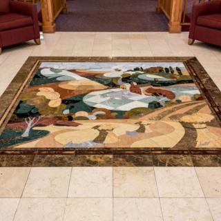 A vibrant floor mosaic featuring a colorful, geometric landscape design within a seating area.