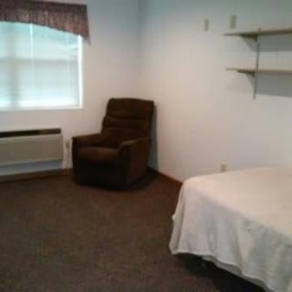 A simple room with a bed, chair, and shelves.