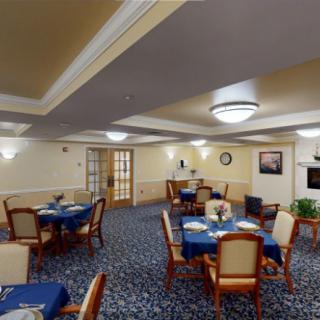 A cozy dining room with neatly arranged tables and chairs, featuring blue tablecloths and warm lighting.