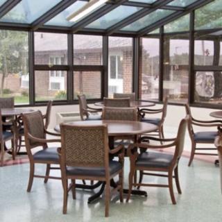 A bright dining area with a glass roof, featuring tables and chairs surrounded by large windows.